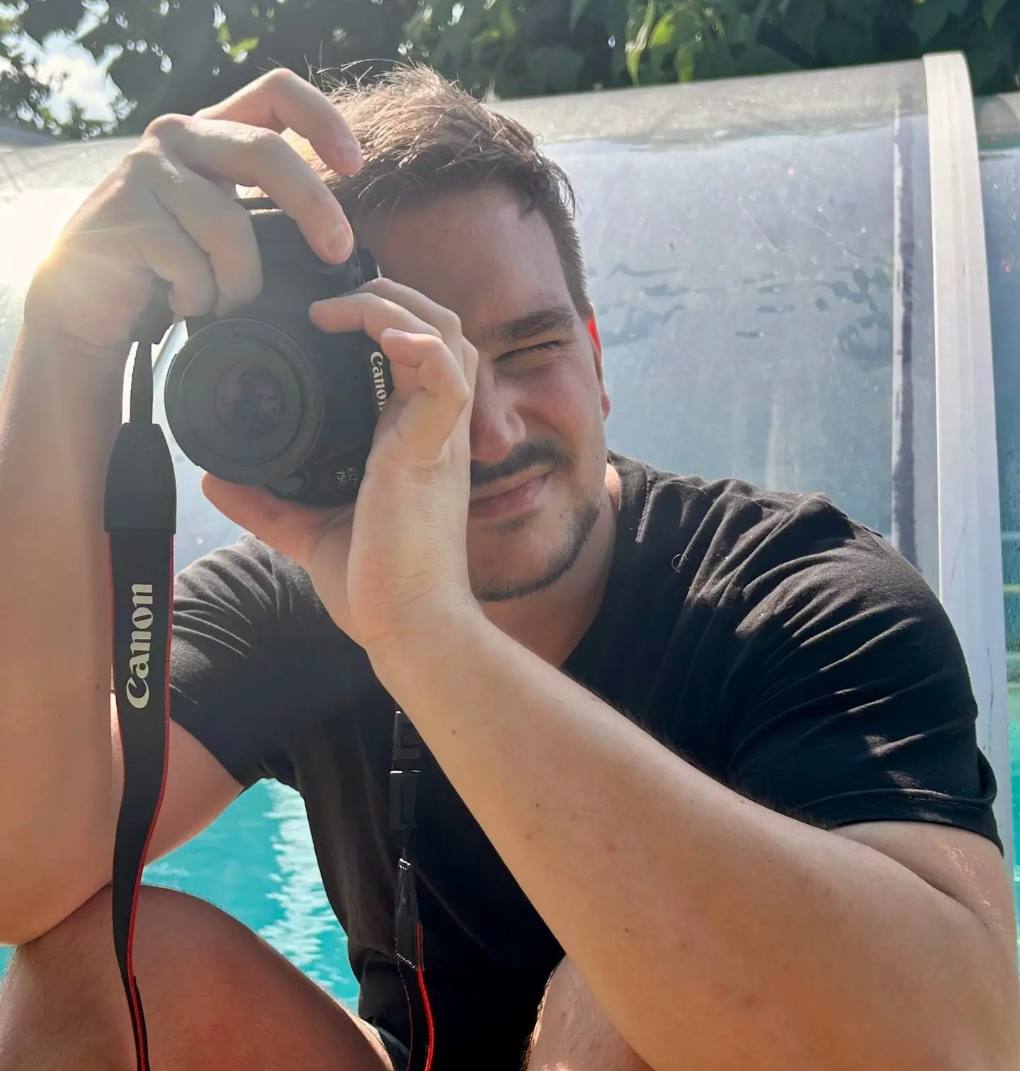 Christoph Suppan hockt vor einem Pool und blickt durch den Sucher einer Kamera